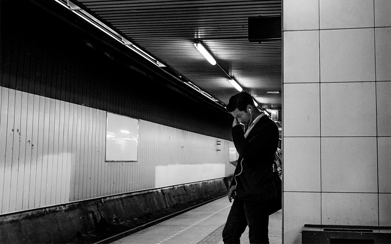 A black and white photo of a man in a subway station wearing earphones.