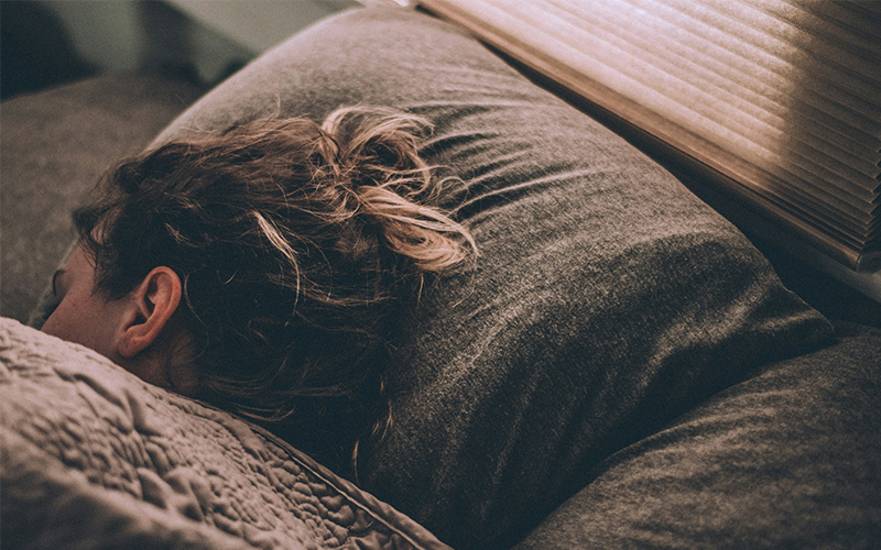 Woman sleeping with head facing the opposite direction to the camera.