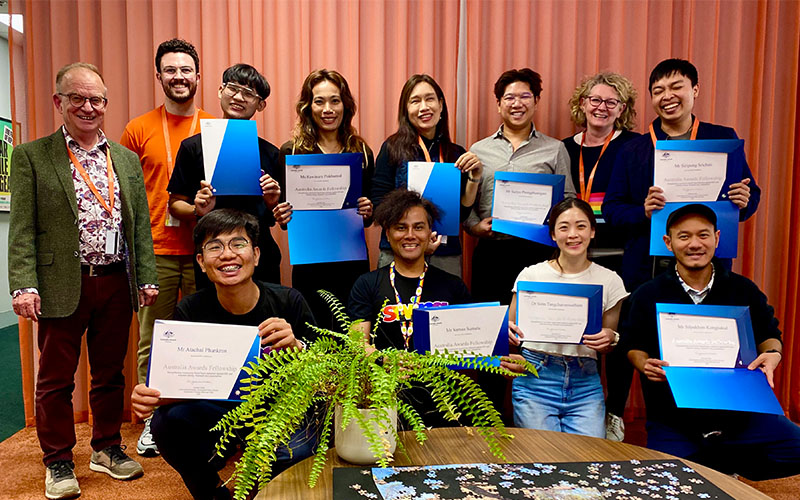 Group photo of Burnet staff and Australia Awards recipients holding blue folders and certificates, standing and sitting in two rows.