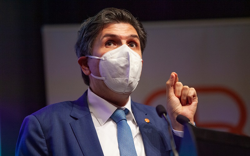 Ziyad wearing a respirator while speaking on stage behind a microphone on a podium.